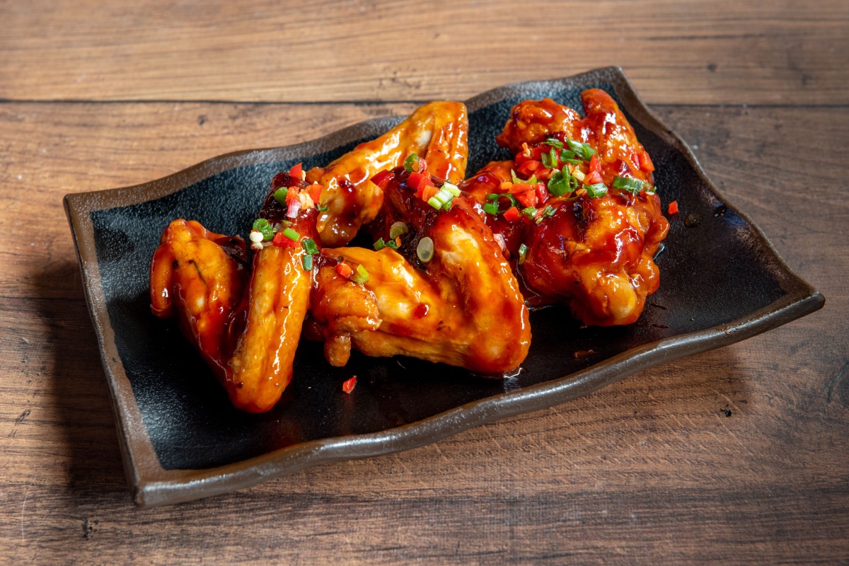 Куриные крылышки в глазури BBQ с зелёным луком и перцем чили на тёмной тарелке